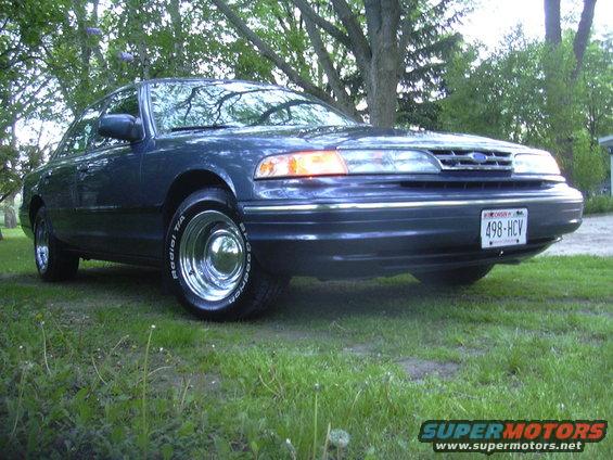 Dark blue sedan with chrome wheels and a Wisconsin license plate 498-HCV parked on grass under trees