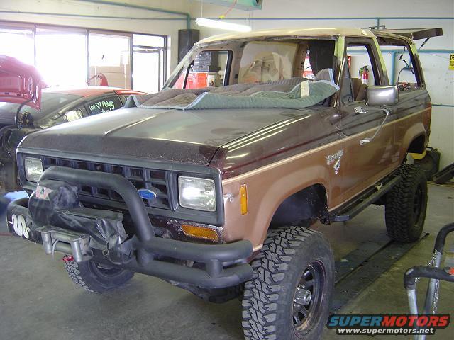 Brown Ford Bronco II with a brush guard and lifted suspension, parked inside a garage with another car visible