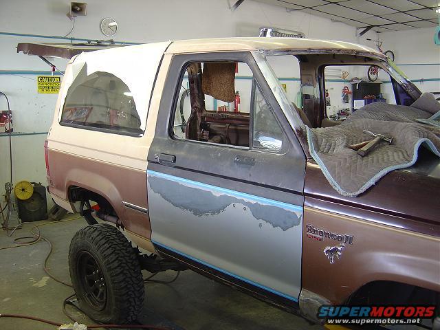 1986 Ford Bronco II in a workshop, undergoing repairs, with primer and body filler visible on the driver's side