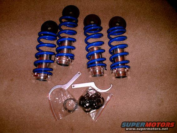 Four blue coilover suspension units with adjustment wrenches and hardware