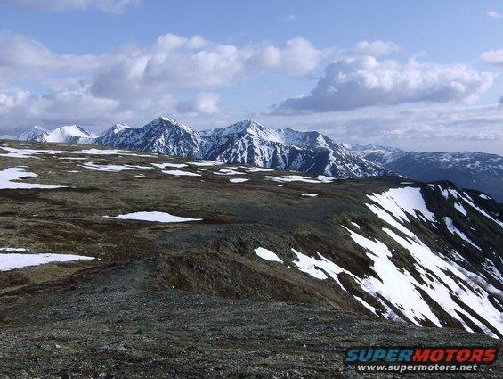 Snow-capped mountains under a cloudy sky, with rocky, snow-dusted terrain in the foreground