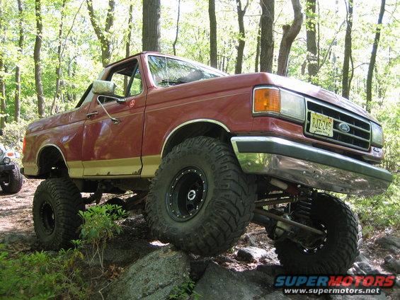 Red 1990 Ford Bronco with lifted suspension and large tires navigating rocks