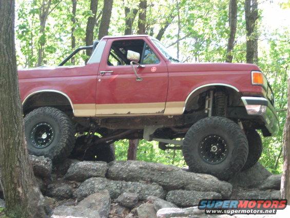Red 1990 Ford Bronco with lifted suspension and large tires navigating a rocky trail