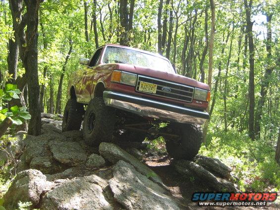 1990 Ford Bronco climbing over large rocks on a wooded trail