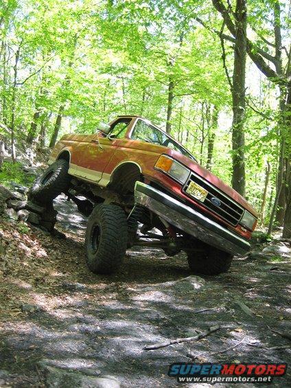 1990 Ford Bronco climbing rocks, front 3/4 view, red and white