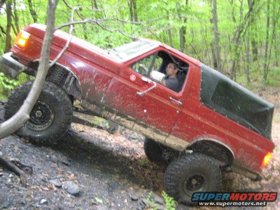 Red 1990 Ford Bronco climbing a muddy incline