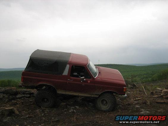Red Ford Bronco with a black soft top, lifted with large tires, parked on a dirt hill
