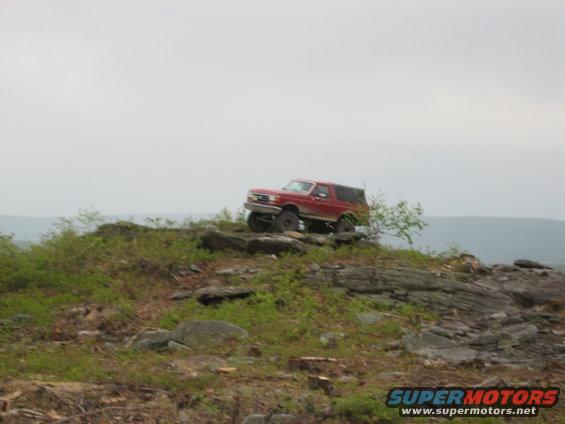 Red SUV on rocky terrain, front 3/4 view, lifted suspension, cloudy sky