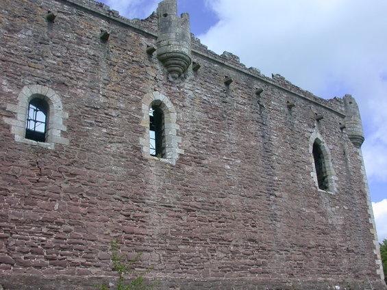 Stone castle wall with arched windows and turrets against a blue sky