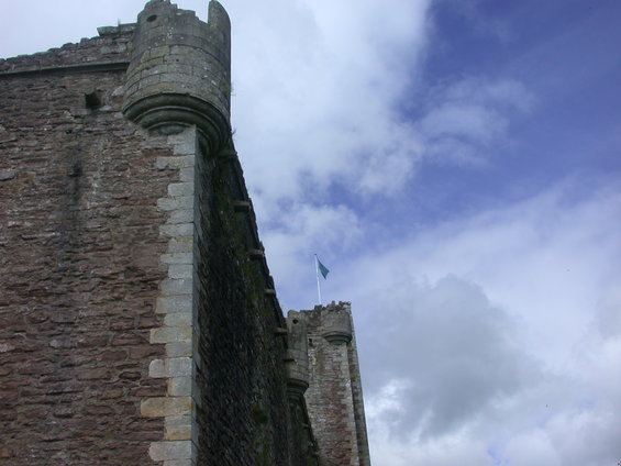 Stone castle wall with turrets and a blue flag against a cloudy sky