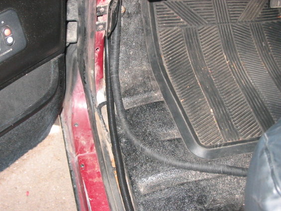 Red car interior door sill with black rubber floor mat and wiring harness