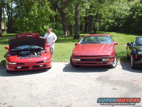 Two red Ford Probes parked outdoors, one with hood open. A man stands by the open hood