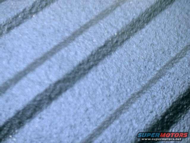 Close-up of a tire tread pattern with diagonal grooves. Supermotors.net logo visible