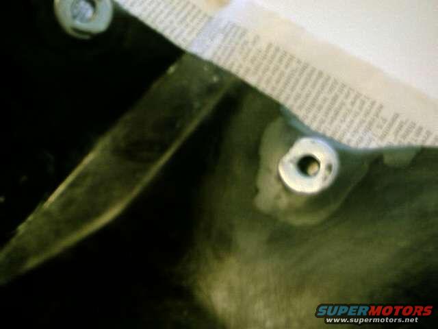 Close-up of a dark car part with masking tape and two bolts. Supermotors.net logo visible