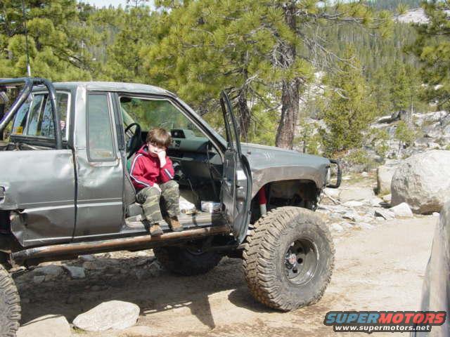 Off-road pickup truck with a child sitting in the driver's seat, door open. Modified suspension and large tires visible