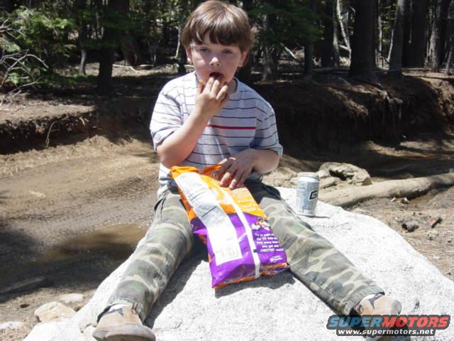 Boy eating chips while sitting on a rock in a wooded area