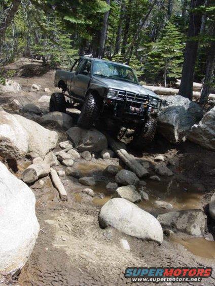 Silver off-road truck with a bull bar navigating a rocky, muddy trail