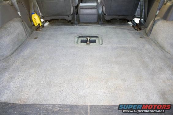 Interior cargo area with gray carpet and rear seats visible. Yellow bottle on the left