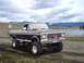 1979 Ford F-250 - A lifted 1979 Ford F-250 pickup truck is parked on a dirt road, with a scenic mountain and lake vista behind it.