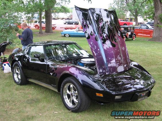 Black Chevrolet Corvette with purple and black flames, hood open, chrome wheels, parked on grass