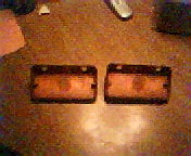 Two amber rectangular automotive turn signal lenses with black housings on a wooden surface