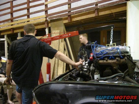 Engine being lowered into a black car with an engine hoist