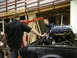 1962 Ford Thunderbird - Mechanics use an engine hoist to carefully lower a V8 engine into the engine bay of a black car during a restoration.