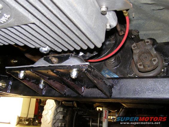 Undercarriage of a vehicle showing transmission, driveshaft, and suspension components. A red wire is visible