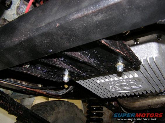 Underbody view of a vehicle showing a transmission pan with 'JEEP' logo and part of a tire and suspension