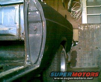 Side view of a black vehicle's rear quarter panel and door frame, showing rust and damage. Part of a truck bed is visible