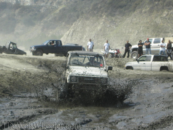 1987 Suzuki Samurai splashing through mud pit with other trucks and ATVs nearby