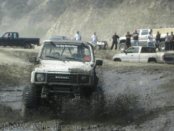 1987 Suzuki Samurai driving through mud, with other trucks visible in the background