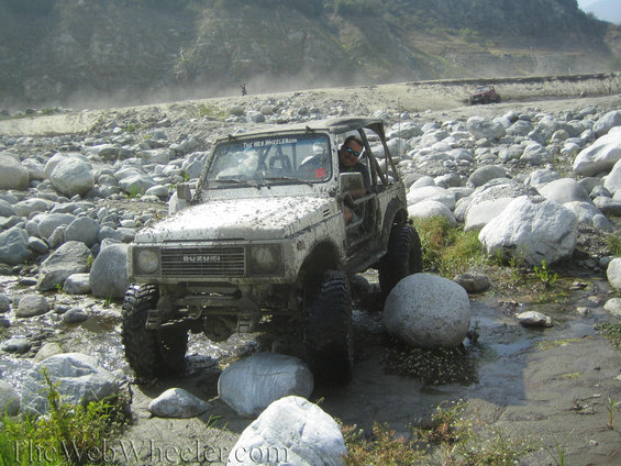 White 1987 Suzuki Samurai navigating a rocky riverbed