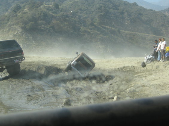 Off-road vehicles stuck in a muddy ditch with people watching