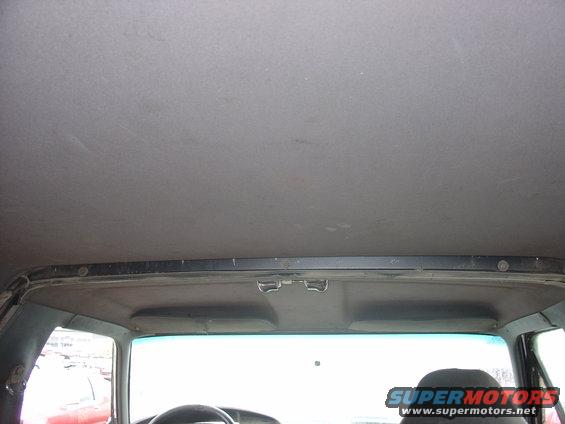Interior view of a car's headliner and upper windshield area. A watermark reads 'SUPERMOTORS.NET'