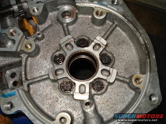 Metal transmission housing with bolts and a central opening. Some oil residue is visible