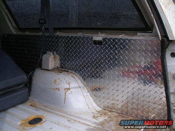 Diamond plate paneling in a dirty white vehicle interior cargo area, showing a seat and wheel well