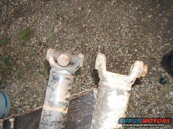 Two driveshafts, one with a U-joint visible, lying on gravel