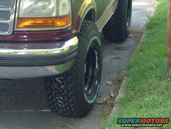 Maroon Ford Bronco front passenger side, chrome bumper, off-road tires, parked on asphalt next to grass