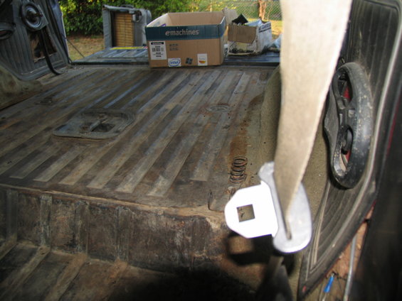 Back of a vehicle with a wood-slat floor, showing a seatbelt buckle and a box in the background