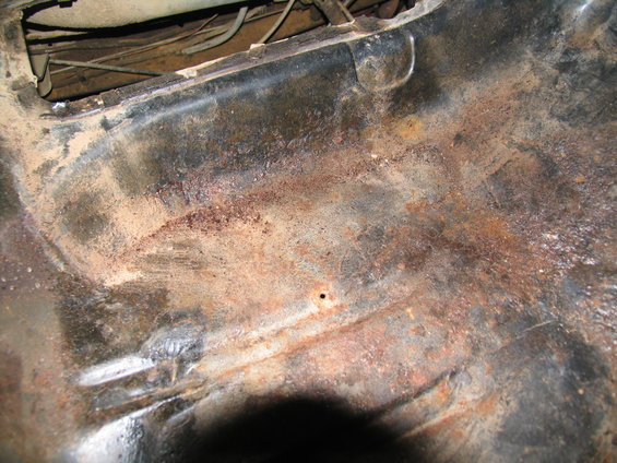 Rusted metal interior floor pan with visible wiring and a small hole