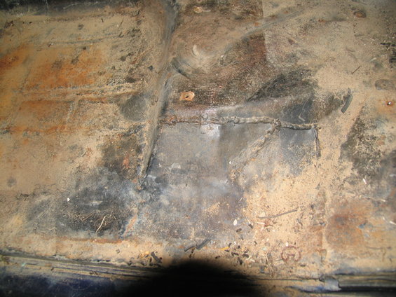 rusted floor pan with visible welds and dirt