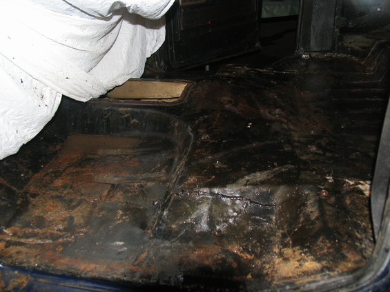 Interior floor of a vehicle, appears to be a truck or SUV, with rust and dirt
