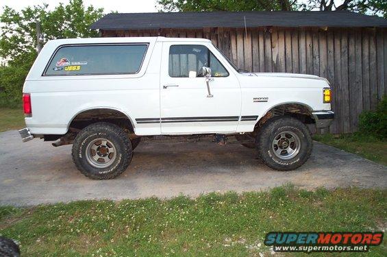 White Ford Bronco with black side stripes, lifted suspension, and off-road tires parked on a concrete driveway