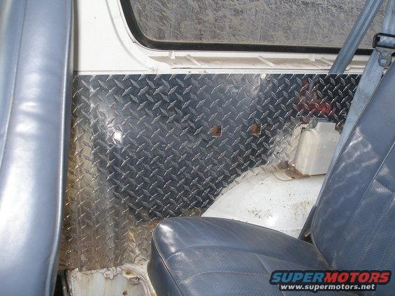 Interior view of a vehicle's rear passenger side, showing a diamond plate panel on the quarter panel and a blue seat