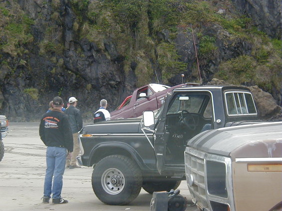 Black Ford pickup truck with open driver door, parked on a sandy beach