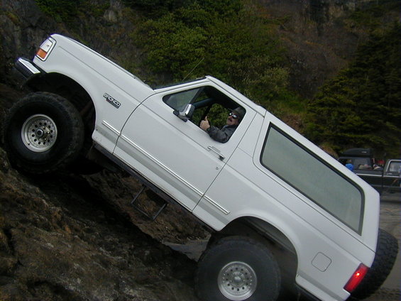 White Ford Bronco with large tires climbing a rocky incline, driver gives a thumbs up