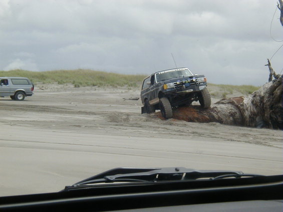 Dark blue SUV with lifted suspension driving over a large log on a sandy beach