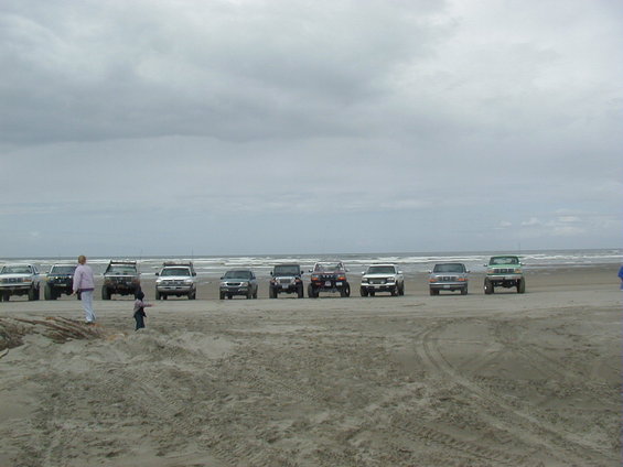 Line of SUVs and trucks on a beach under a cloudy sky