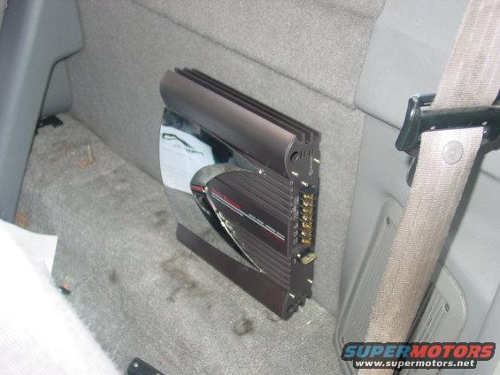 Car amplifier mounted on gray carpeted interior wall next to a seatbelt